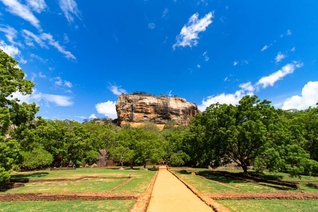 The rock fortress of Sigiriya rising out of flat green jungle in Sri Lanka's Cultural Triangle.