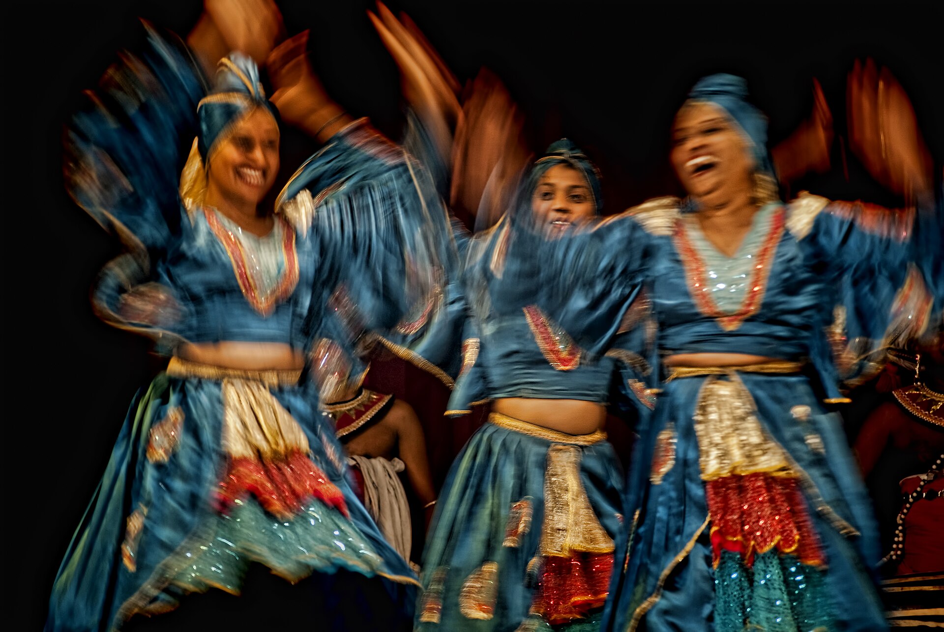 Kandyan dancers in blue and gold costumes mid-movement against a dark stage.