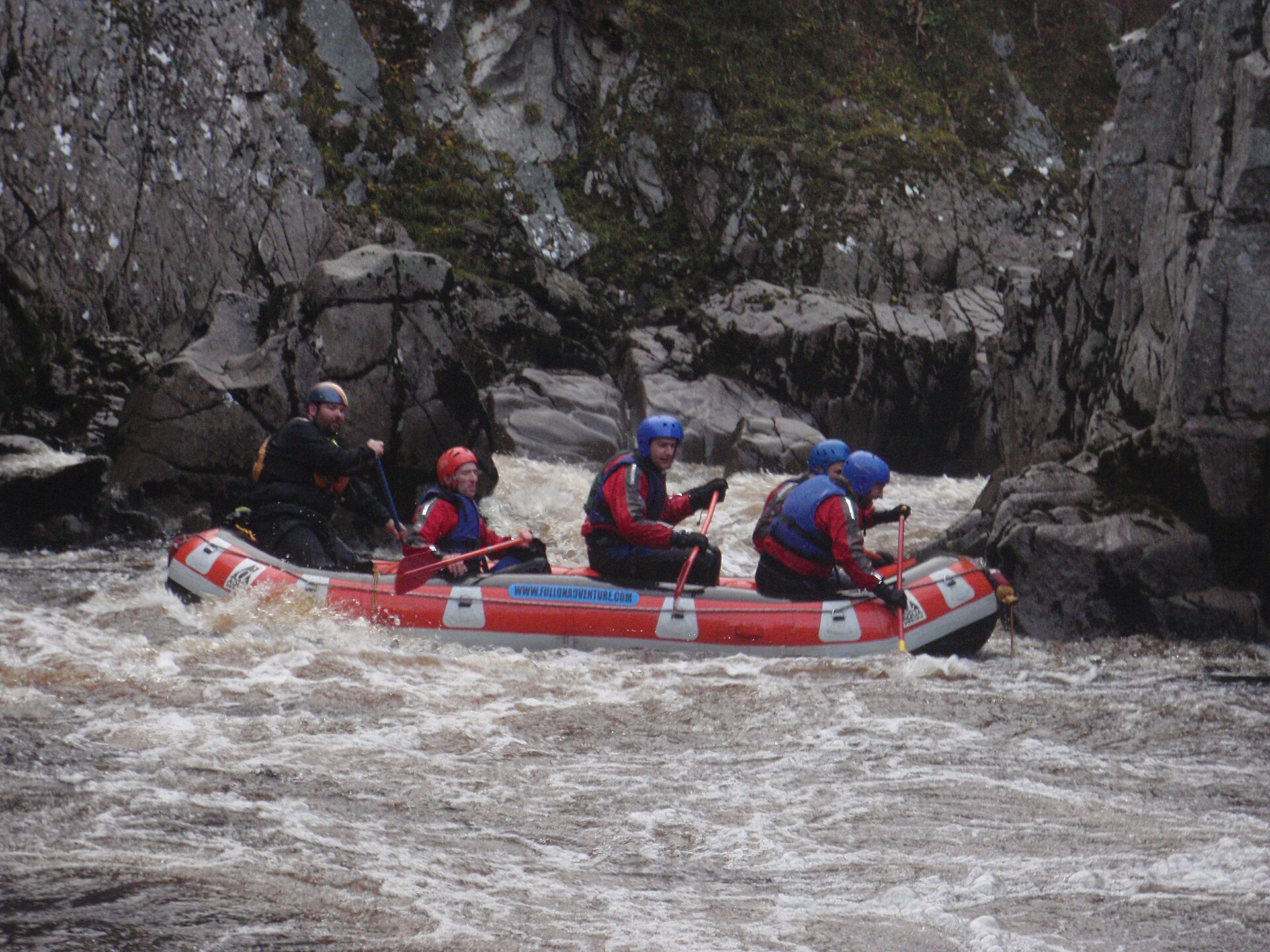 A raft crew paddling through white water on a forested river.